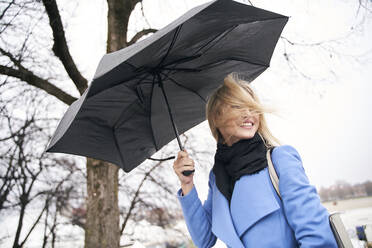 Smiling blond woman holding umbrella in storm - PNEF02504