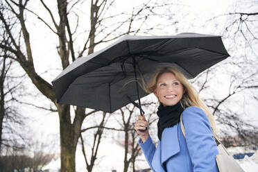 Smiling blond woman holding umbrella in storm - PNEF02505