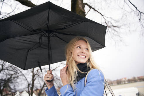 Smiling blond woman holding umbrella outdoors - PNEF02507
