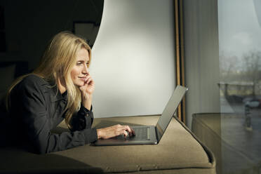 Blonde Frau auf dem Sofa liegend mit Laptop - PNEF02510