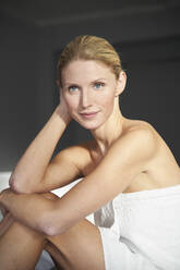 Portrait of beautiful woman wrapped in a towel sitting on bed - PNEF02530
