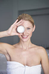 Portrait of smiling beautiful woman holding cream jar in front of her eye - PNEF02545