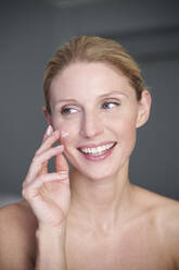 Portrait of happy beautiful woman applying cream on her cheek - PNEF02551