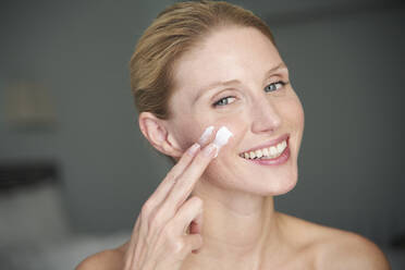 Portrait of happy beautiful woman applying cream on her cheek - PNEF02552