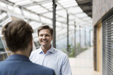 Businessman talking to colleague in atrium of office building - JOSEF00120