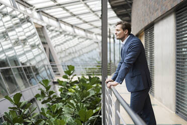 Businessman standing on gallery, enjoying green plants in atrium - JOSEF00121