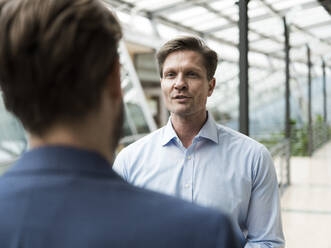 Businessman talking to colleague in atrium of office building - JOSEF00128