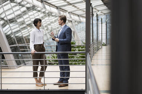 Geschäftsmann und Frau im Gespräch in einem nachhaltigen Bürogebäude, mit digitalem Tablet, lizenzfreies Stockfoto