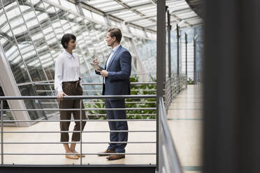 Businessman and woman talking in sustainable office building, using digital tablet - JOSEF00137