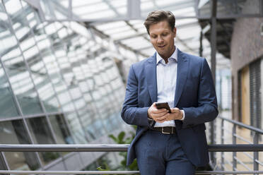 Businessman using smartphone in bright atrium - JOSEF00148