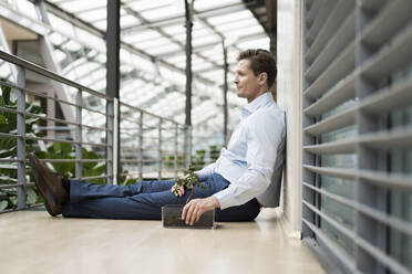 Businessman in green atrium, sitting on gallery - JOSEF00156