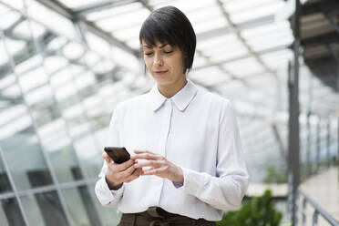 Geschäftsfrau mit Smartphone im Atrium eines Bürogebäudes - JOSEF00159