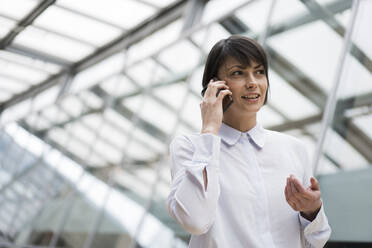 Geschäftsfrau mit Smartphone im Atrium eines Bürogebäudes - JOSEF00164