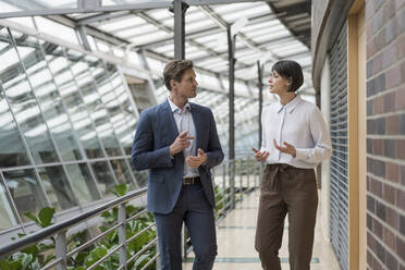 Businessman and woman talking in sustainable office building - JOSEF00166