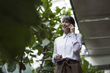 Successful businesswoman talking on the phone in a sustainable office building - JOSEF00167