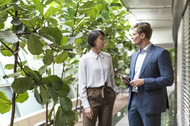 Geschäftsmann und Frau im Gespräch in einem nachhaltigen Bürogebäude, mit digitalem Tablet - JOSEF00181