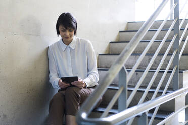 Geschäftsfrau, die auf einer Treppe sitzt und ein digitales Tablet benutzt - JOSEF00182