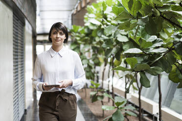 Successful businesswoman walking on gallery of sustainable office building, holding digital tablet - JOSEF00184