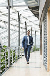 Confident businessman walking on gallery of green atrium - JOSEF00195