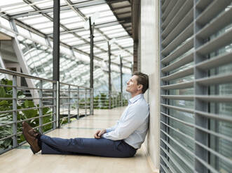 Businessman in green atrium, sitting on gallery, thinking - JOSEF00219