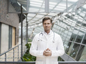 Portrait of doctor with stethoscope, standing in atrium - JOSEF00223