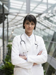 Portrait of femeale doctor with stethoscope, standing in atrium, with arms crossed - JOSEF00228