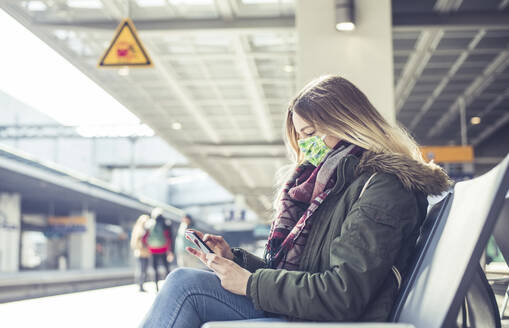 Junge Frau mit Smartphone und Maske auf dem Bahnsteig - BFRF02205