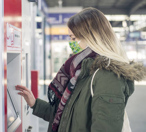 Young woman wearing mask using ticket machine at the station stock photo