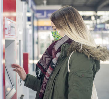 Young woman wearing mask using ticket machine at the station - BFRF02210
