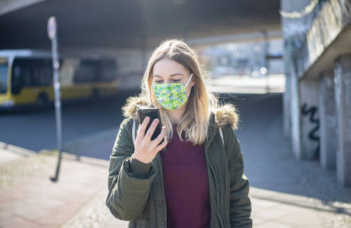 Junge Frau mit Smartphone und Maske in der Stadt - BFRF02213