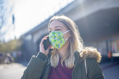 Porträt einer jungen Frau, die eine Maske trägt und in der Stadt telefoniert - BFRF02214