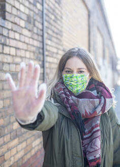 Porträt einer jungen Frau mit Maske, die ihre Hand hebt - BFRF02218