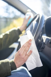 Nahaufnahme einer Frau im Auto beim Desinfizieren des Lenkrads - BFRF02220