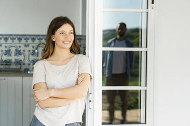 Smiling young woman leaning onto door looking at her boyfriend standing outside - SBOF02144