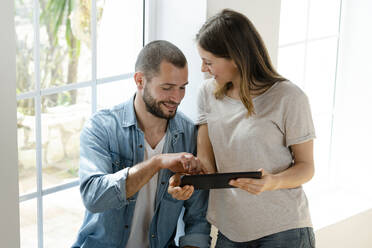 Smiling couple at home in front of window looking at tablet together - SBOF02162