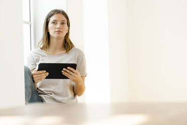 Seriöse junge brünette Frau zu Hause sitzt auf Fensterbank und hält ihr Tablet - SBOF02164