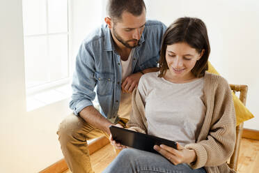 Young couple at home in front of window looking at tablet together - SBOF02178