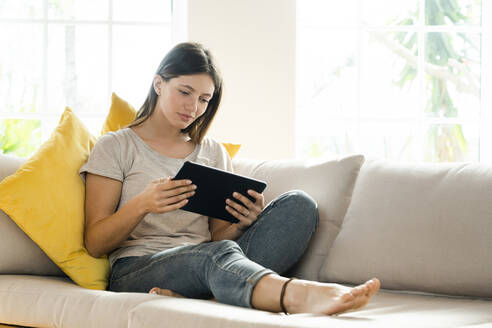 Ernste brünette Frau entspannt sich auf der Couch und schaut auf ihr Tablet - SBOF02194