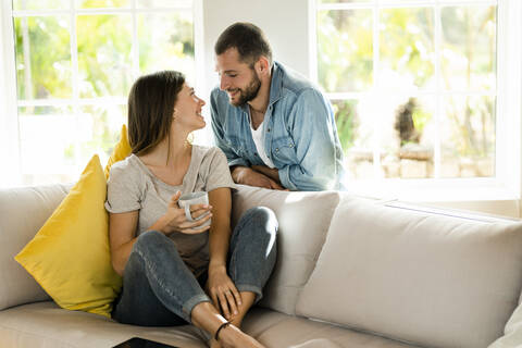 Verliebtes Paar, das sich zu Hause auf der Couch anlächelt, lizenzfreies Stockfoto