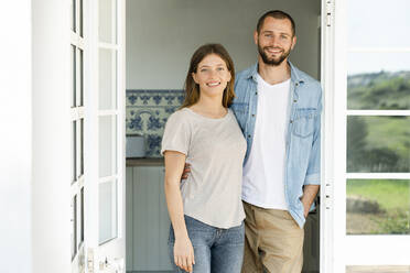 Attraktives junges Paar, das zusammen zu Hause in der Tür steht und lächelt - SBOF02207