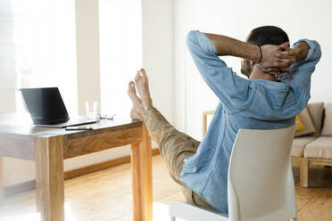 Junger Mann arbeitet zu Hause im Home Office und entspannt sich im modernen Wohnzimmer mit den Füßen auf dem Tisch - SBOF02216