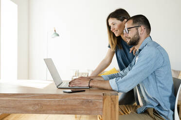 Lächelndes Paar arbeitet am Laptop von zu Hause aus im Home Office im modernen Wohnzimmer - SBOF02218