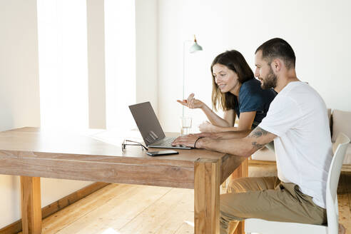 Junges Paar arbeitet am Laptop von zu Hause aus im Home Office im modernen Wohnzimmer - SBOF02220
