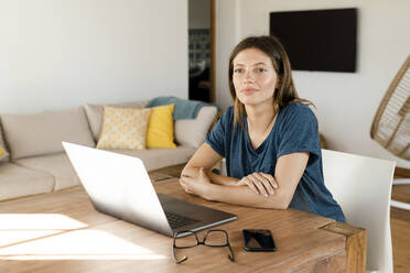 Junge Frau arbeitet am Laptop von zu Hause aus im Heimbüro im modernen Wohnzimmer - SBOF02224