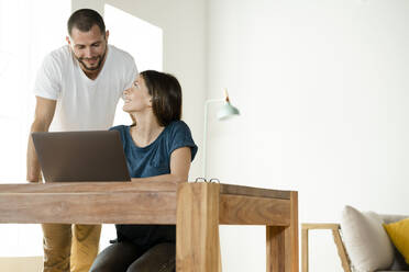 Lächelndes Paar arbeitet am Laptop von zu Hause aus im Home Office im modernen Wohnzimmer - SBOF02233