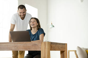 Glückliches Paar arbeitet am Laptop von zu Hause aus im Heimbüro im modernen Wohnzimmer - SBOF02234