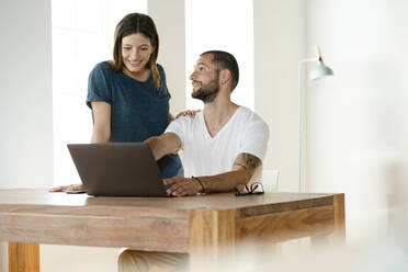 Smiling couple working at laptop from home in home office in modern living room - SBOF02235