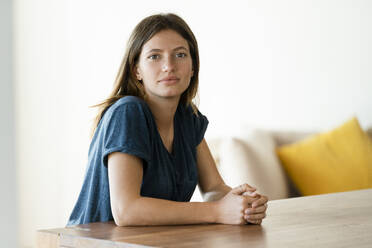 Portrait of confident young woman sitting at table at home - SBOF02242