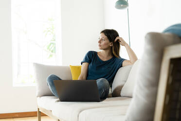 Young woman sitting on couch at home with laptop - SBOF02243