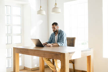 Young man at home working on his laptop in home office in modern living room - SBOF02248